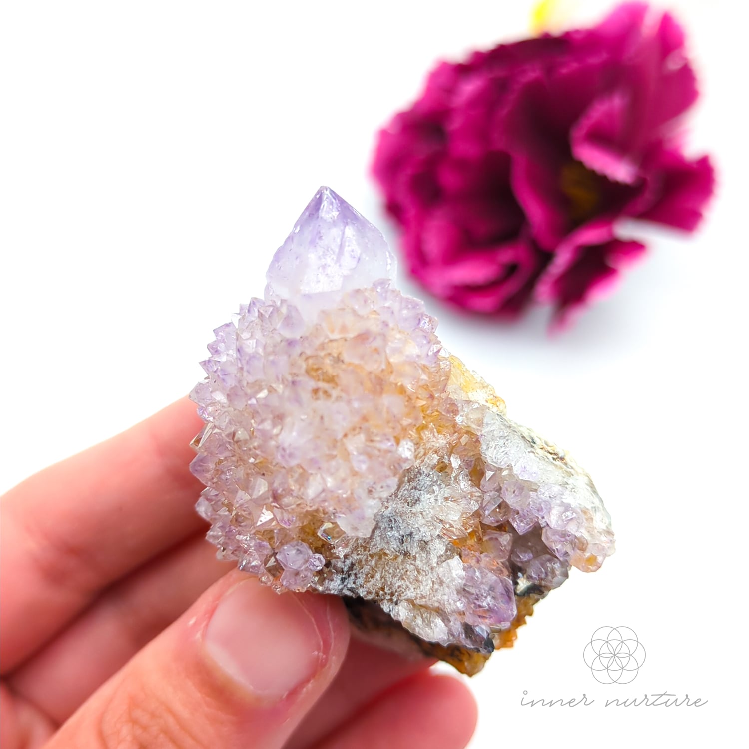 Crystal rock held in a hand with a blurred pink flower in the background. Spirit Quartz cluster for sale at Inner Nurture, an online crystal shop in Australia.