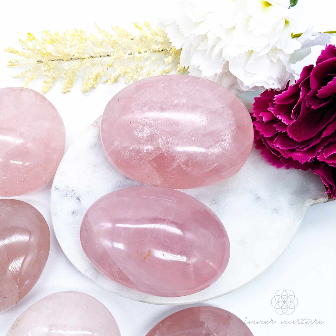 rose quartz palm stones to hold for love, compassion and heart chakra healing. sitting on a marble background with flowers. sold at inner nurture, an australian online crystal shop
