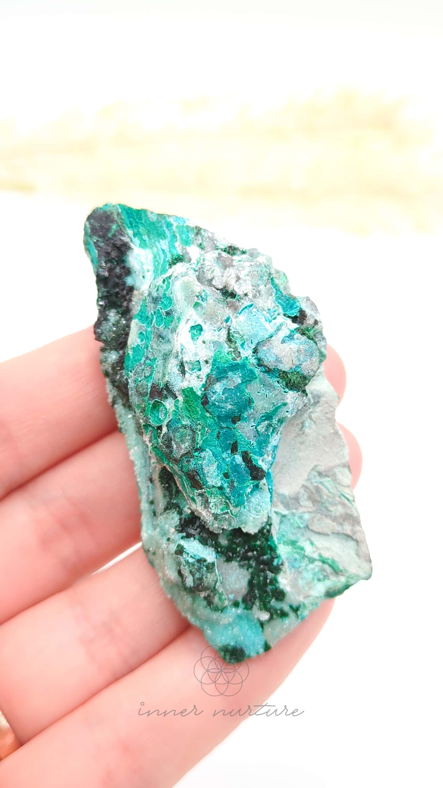 Turquoise crystal held in a hand with a blurred yellow background. Malacolla Specimen, Drusy Coated On Dolomite - #2 at Crystal Shop Online Australia called Inner Nurture