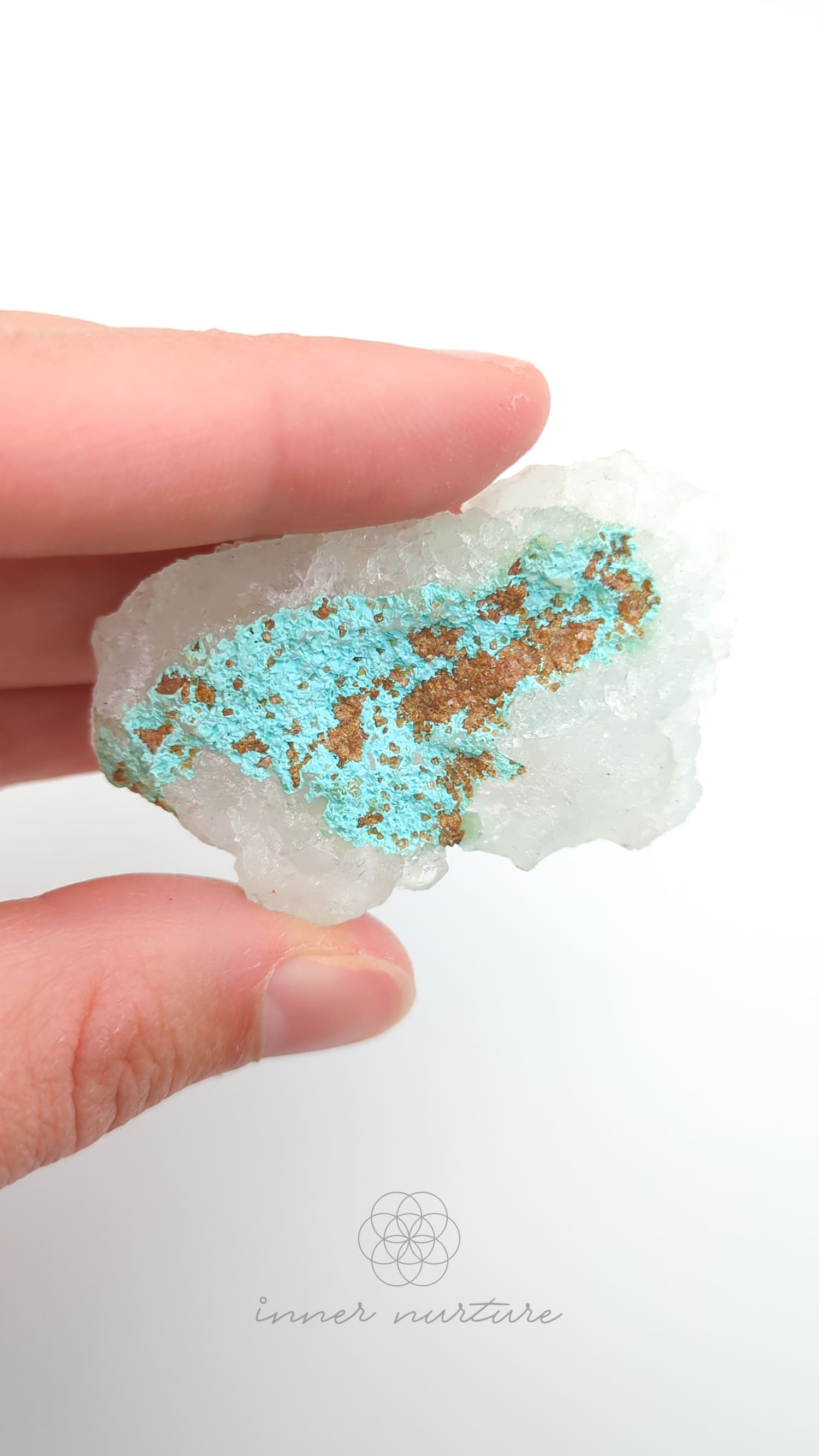Hand holding a crystal with blue and brown mineral deposits on a white background. Malacolla Specimen, Drusy Coated On Dolomite - #17 at Crystal Shop Online Australia called Inner Nurture