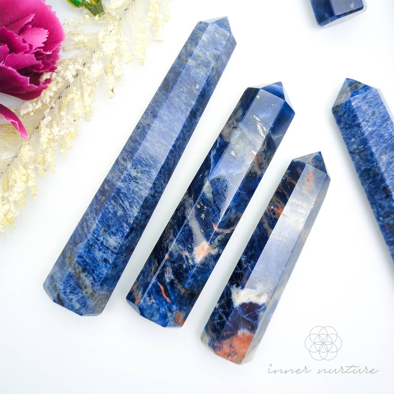 Blue crystal sticks with marbled patterns on a white background, featuring a pink flower. Sodalite Generator Tower available to Buy from Inner Nurture - an online Crystals shop in Australia