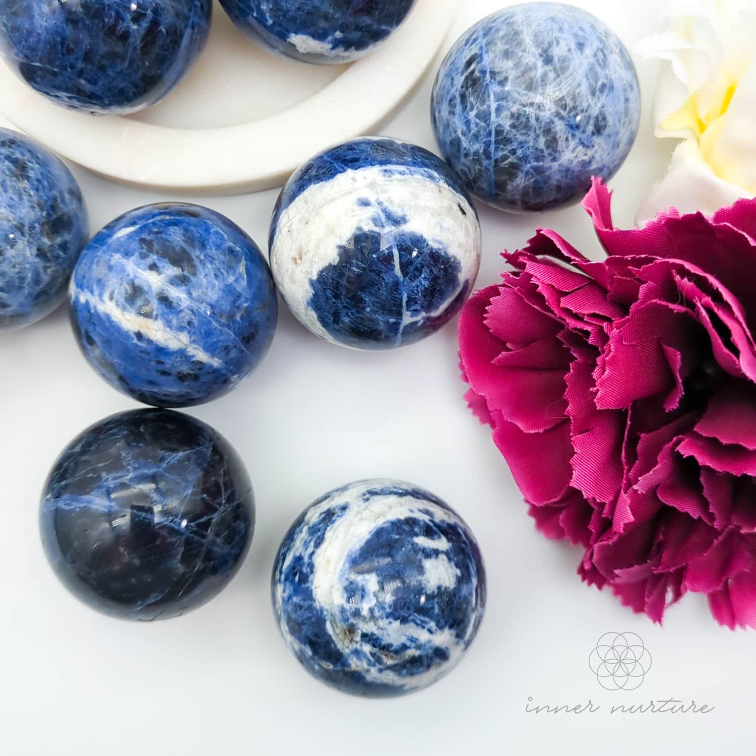 Blue and white marbled stones on a white surface with a pink flower.  Sodalite Sphere sold at inner nurture, an australian online crystal shop