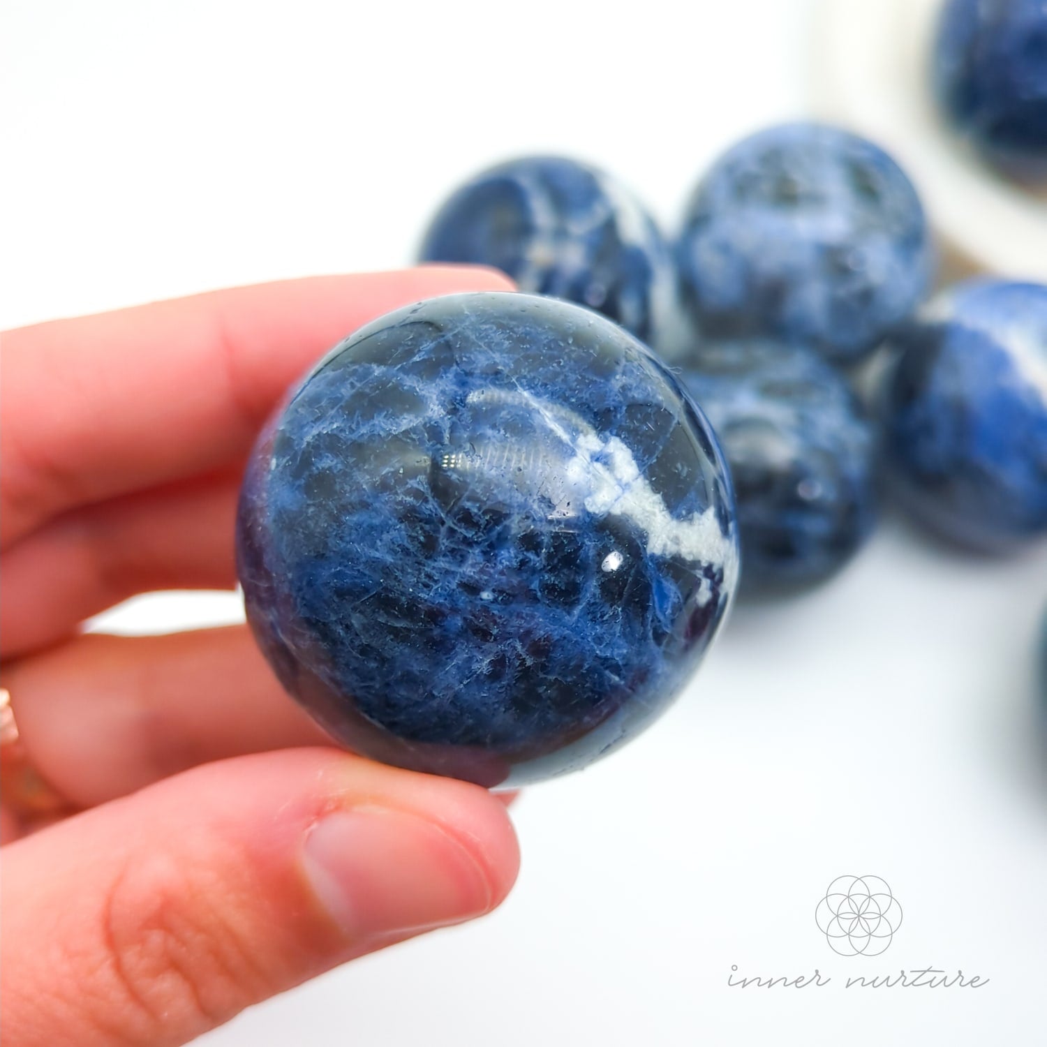 Blue and white marbled stones held in a hand with more stones in the background. Sodalite Sphere sold at inner nurture, an australian online crystal shop