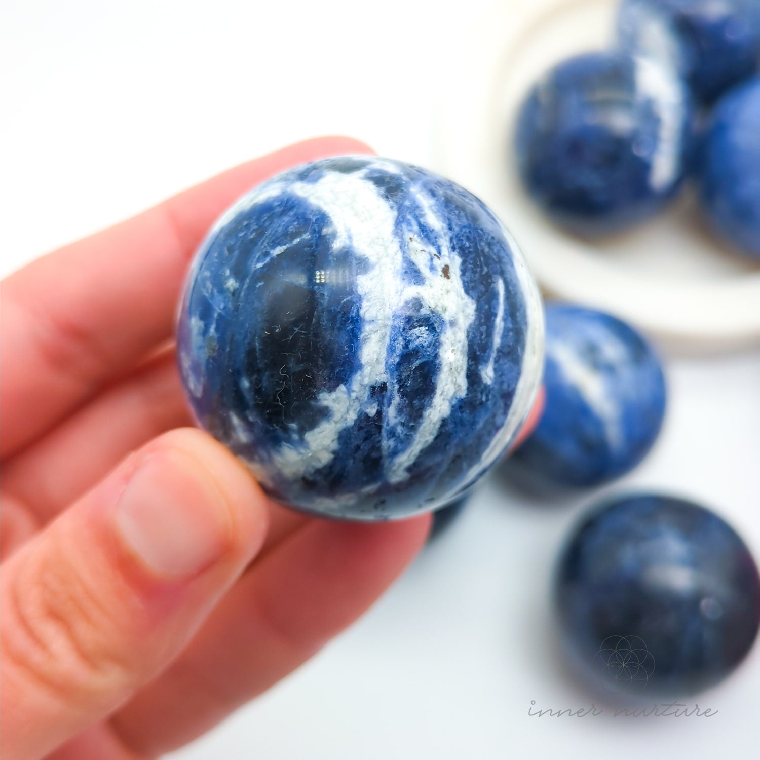 Blue and white marbled stones held in a hand with more stones in the background. Sodalite Sphere sold at inner nurture, an australian online crystal shop