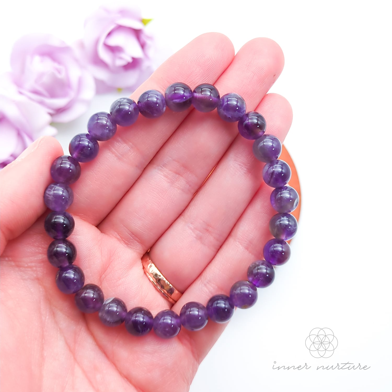 Purple beaded bracelet on a wooden surface with flowers in the background. Multicolored beaded bracelet on a wooden surface with flowers in the background. Blue beaded bracelet on a wooden disc with pink flowers in the background. Amethyst bead bracelet sold by Inner Nurture, an online crystal shop in Australia. 