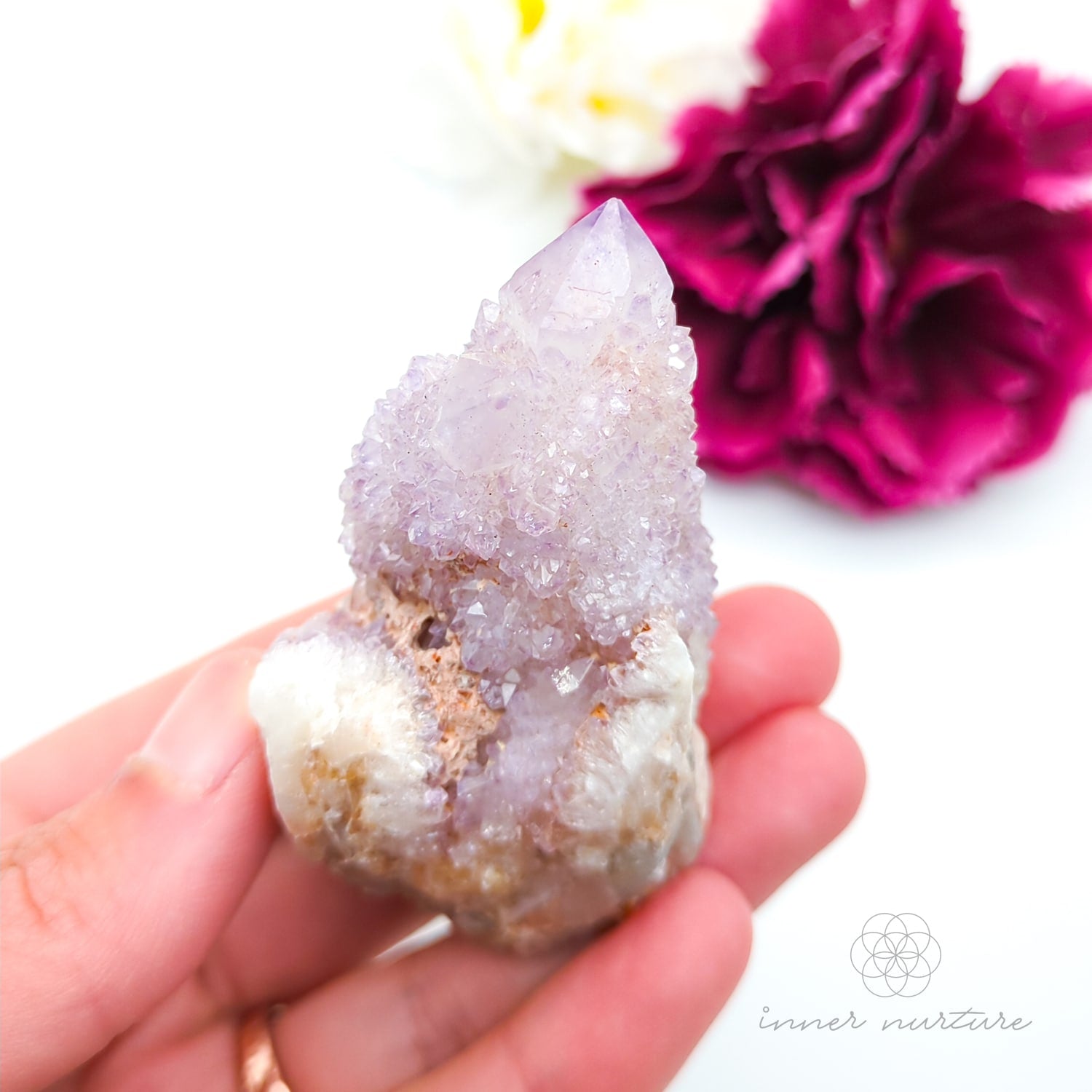 Crystal rock held in a hand with a blurred pink flower in the background. Spirit Quartz cluster for sale at Inner Nurture, an online crystal shop in Australia. 