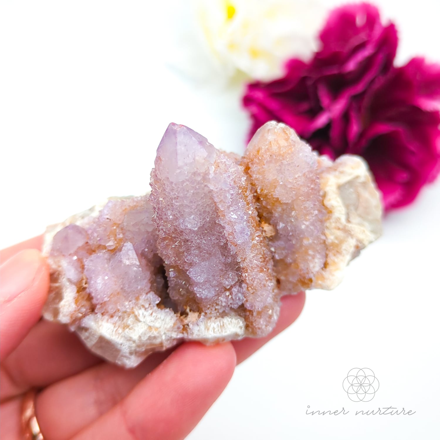 Crystal rock held in a hand with a blurred pink flower in the background. Spirit Quartz cluster for sale at Inner Nurture, an online crystal shop in Australia. 