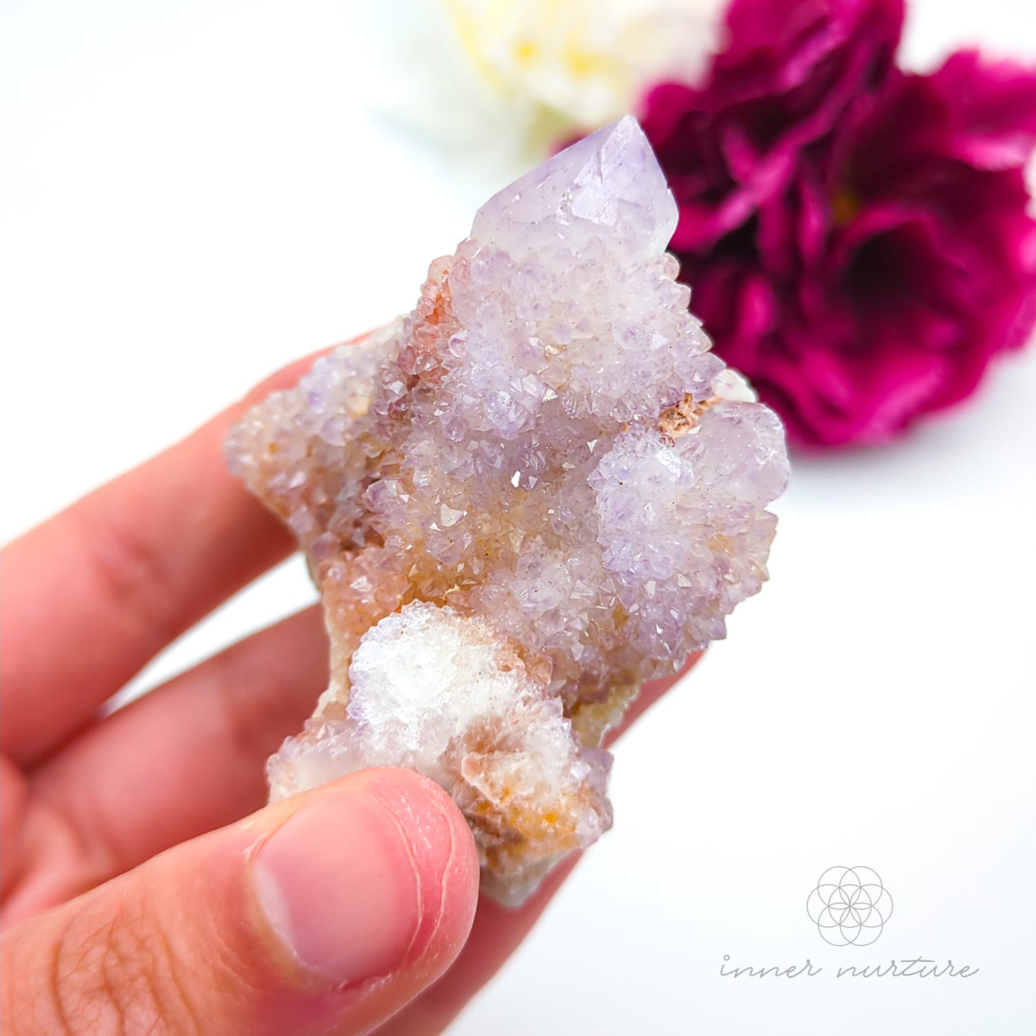 Crystal rock held in a hand with a blurred pink flower in the background. Spirit Quartz cluster for sale at Inner Nurture, an online crystal shop in Australia. 