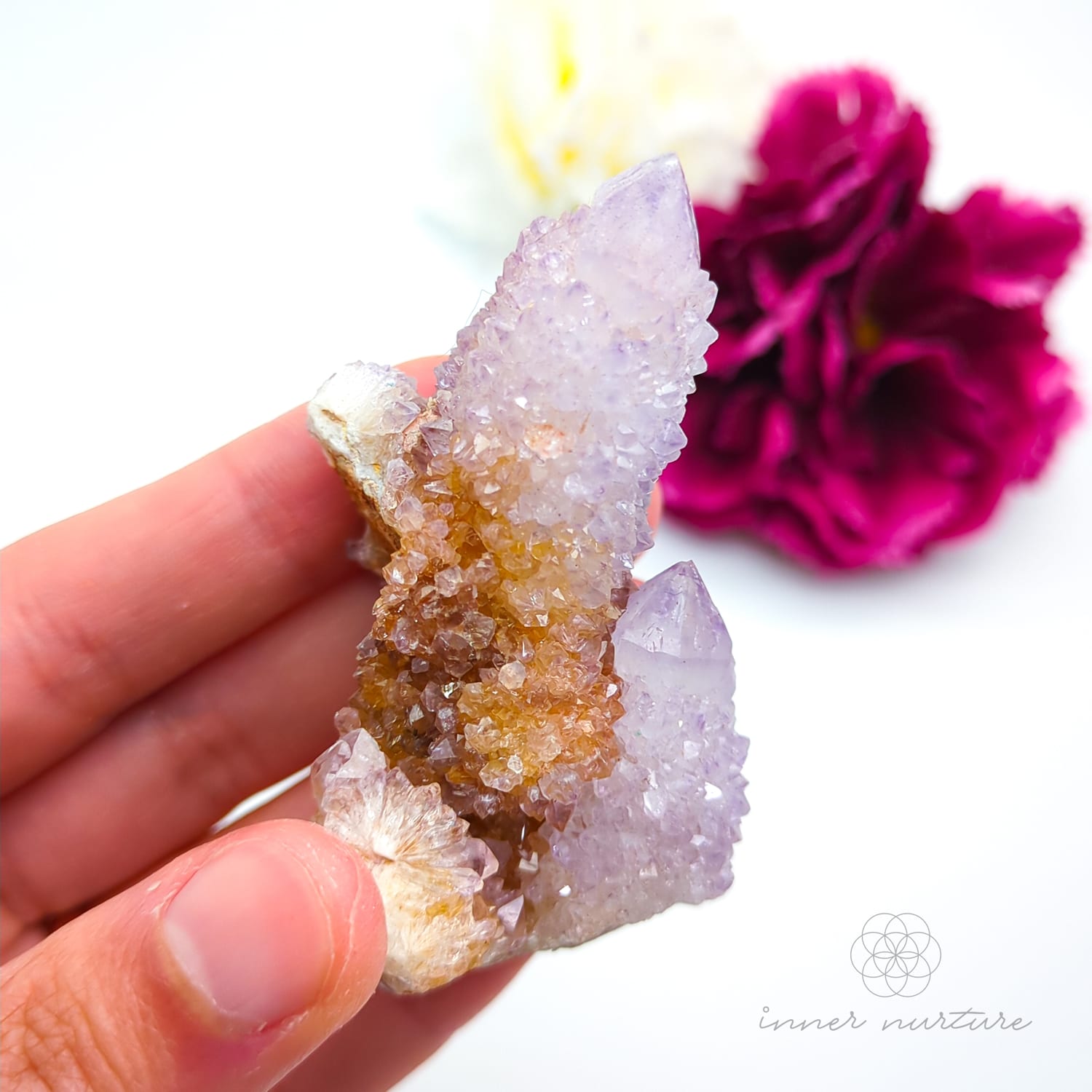 Crystal rock held in a hand with a blurred pink flower in the background. Spirit Quartz cluster for sale at Inner Nurture, an online crystal shop in Australia. 