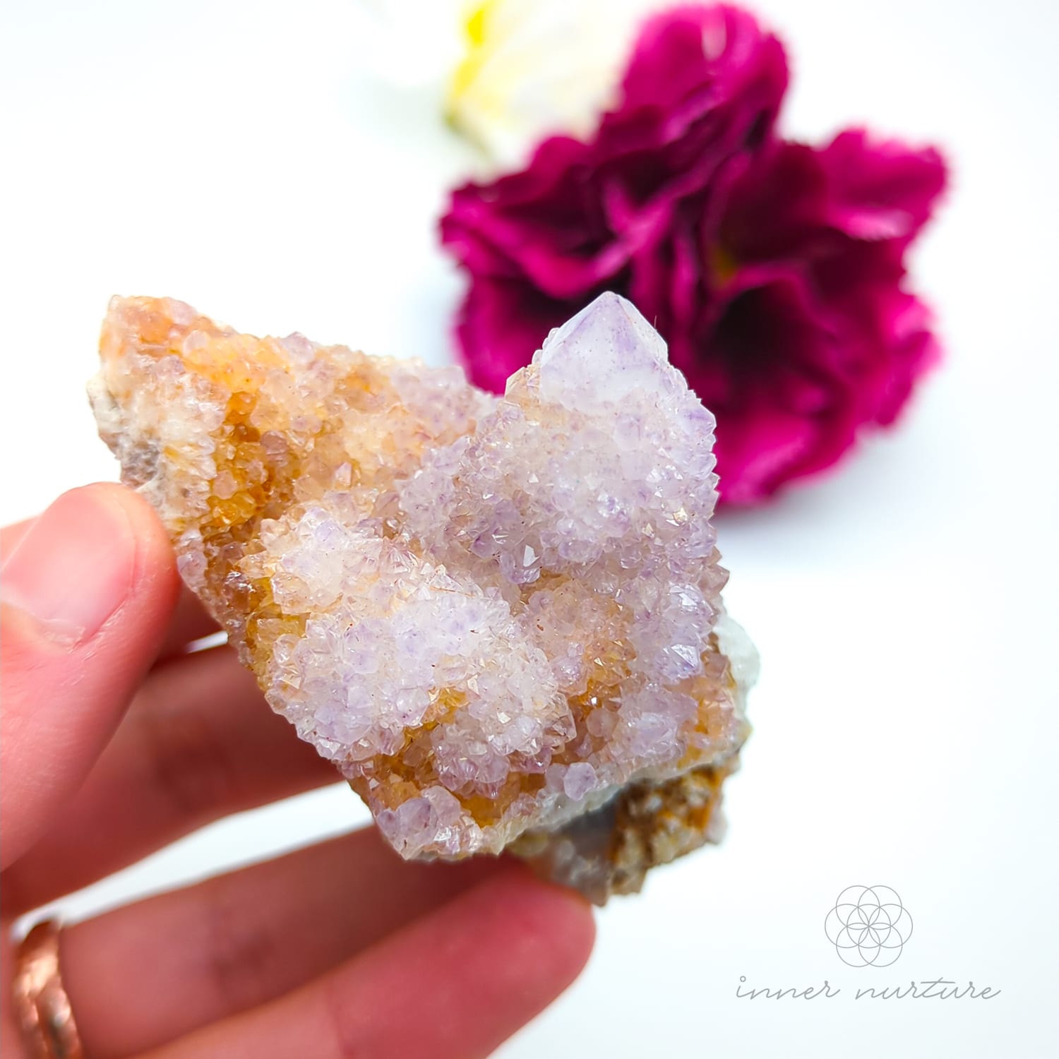 Crystal rock held in a hand with a blurred pink flower in the background. Spirit Quartz cluster for sale at Inner Nurture, an online crystal shop in Australia. 