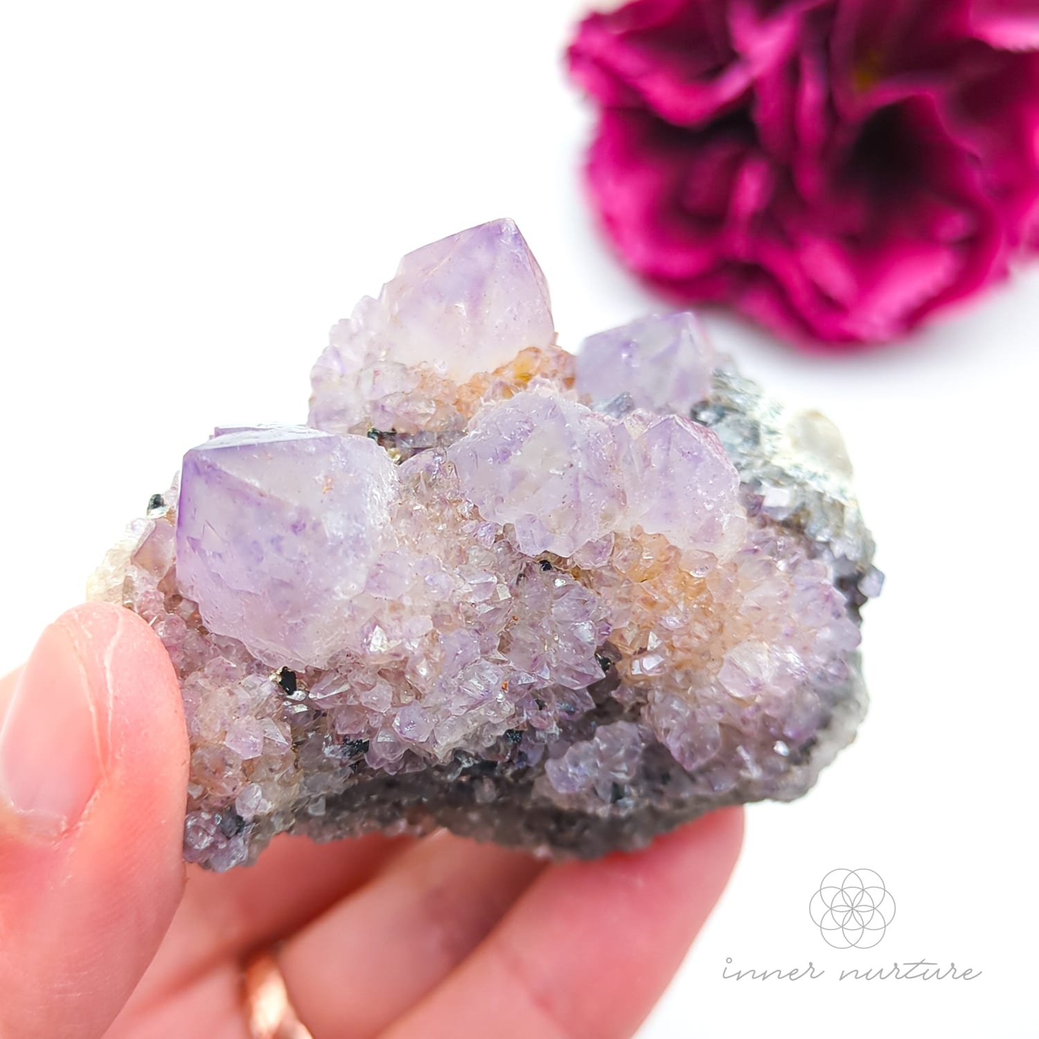 Crystal rock held in a hand with a blurred pink flower in the background. Spirit Quartz cluster for sale at Inner Nurture, an online crystal shop in Australia. 