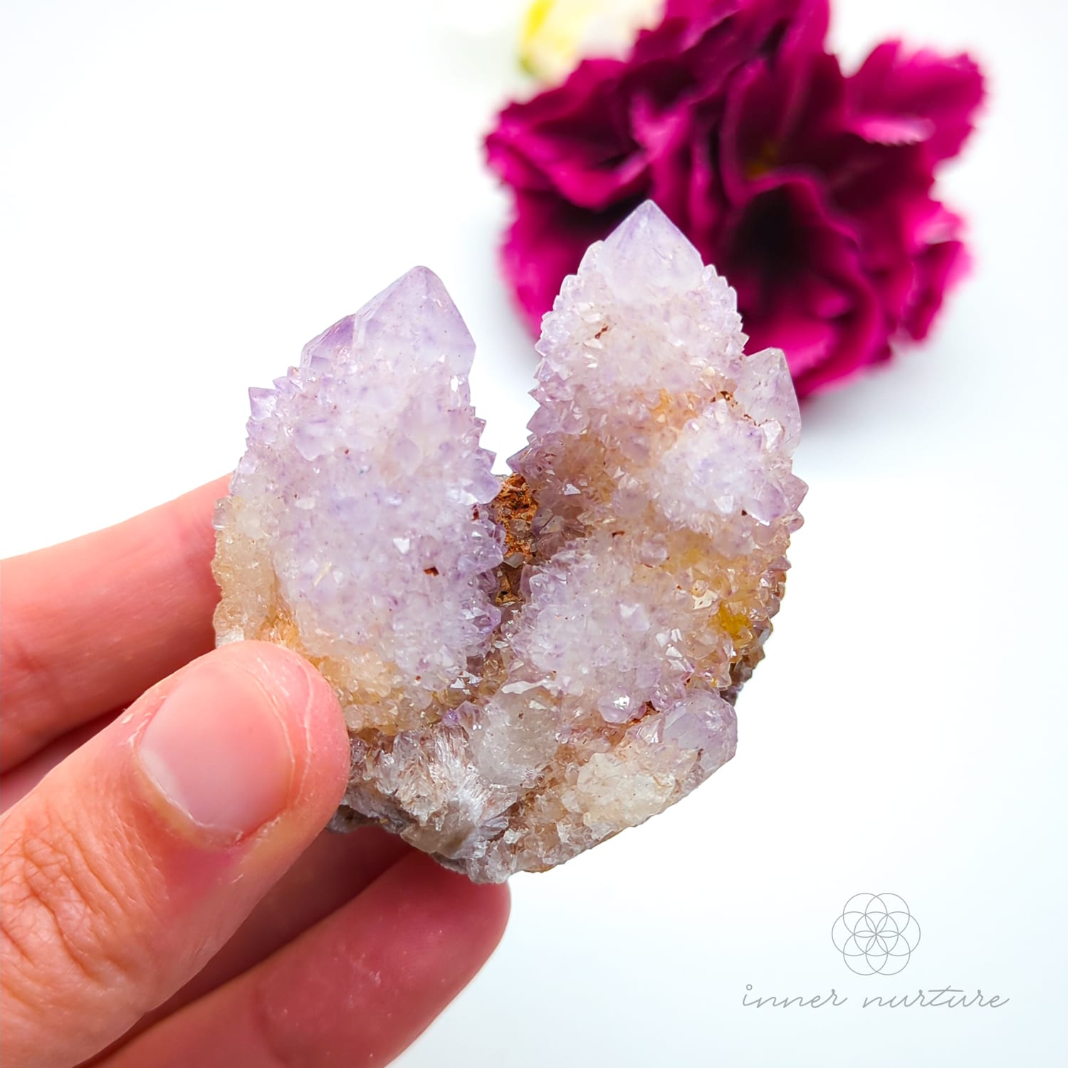 Crystal rock held in a hand with a blurred pink flower in the background. Spirit Quartz cluster for sale at Inner Nurture, an online crystal shop in Australia. 