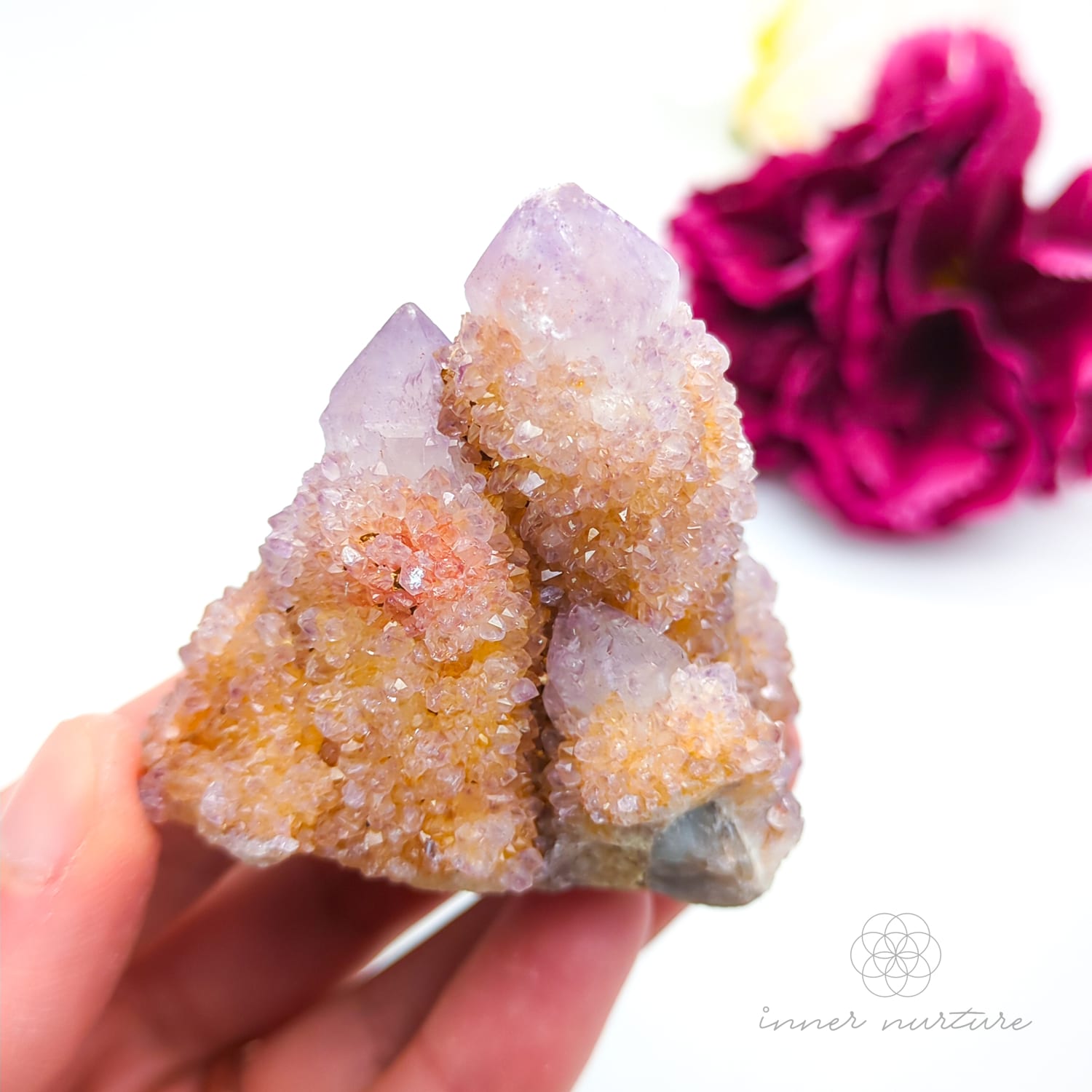 Crystal rock held in a hand with a blurred pink flower in the background. Spirit Quartz cluster for sale at Inner Nurture, an online crystal shop in Australia. 