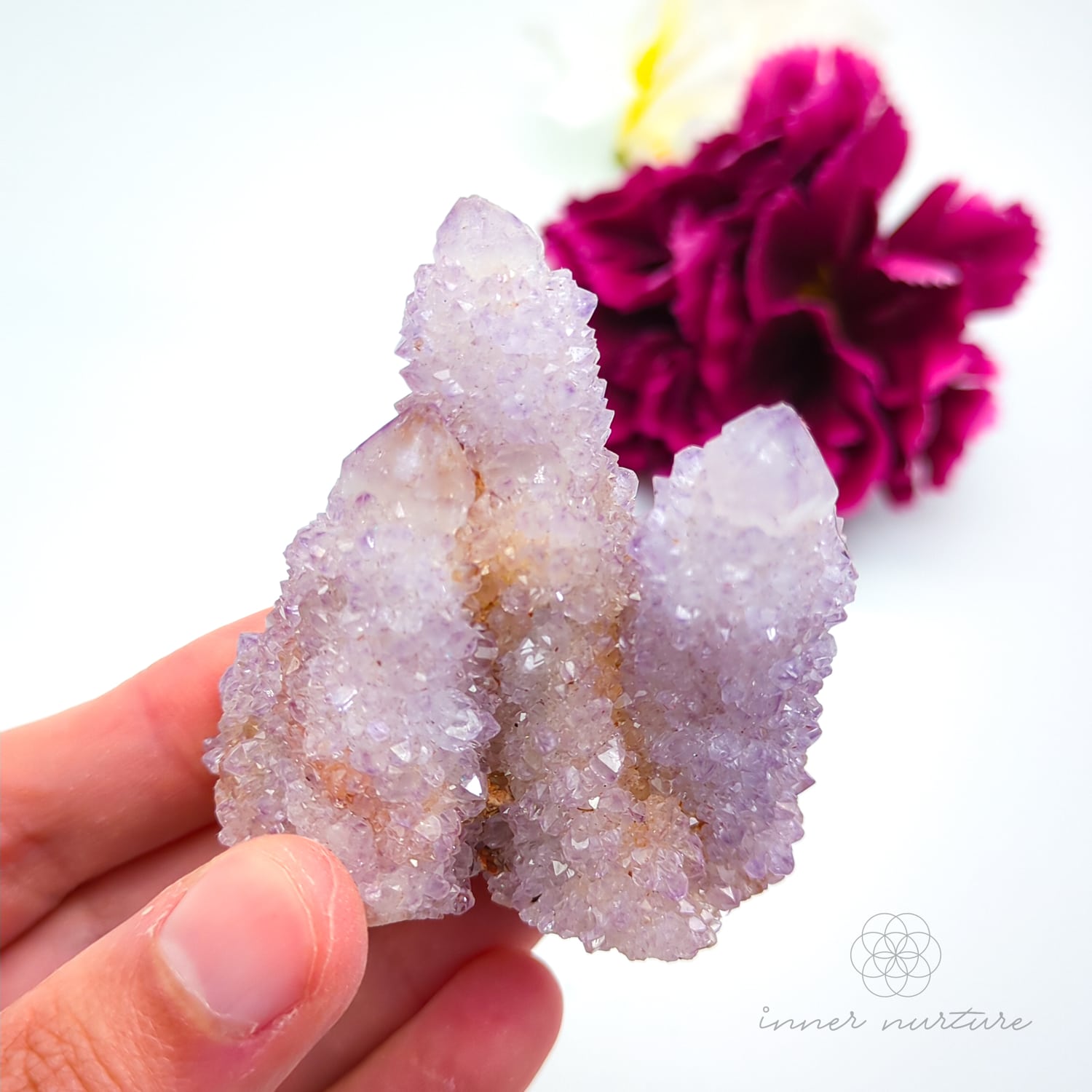 Crystal rock held in a hand with a blurred pink flower in the background. Spirit Quartz cluster for sale at Inner Nurture, an online crystal shop in Australia. 