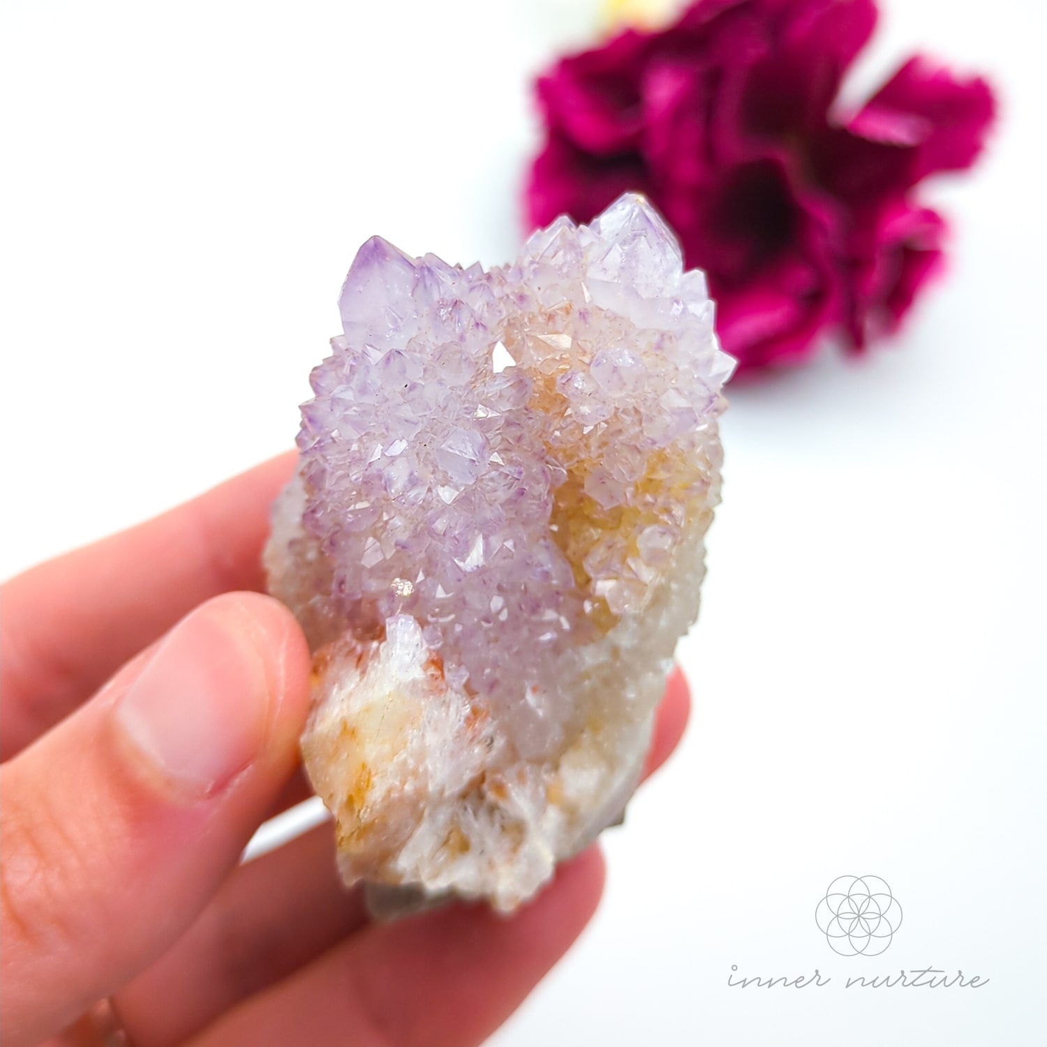 Crystal rock held in a hand with a blurred pink flower in the background. Spirit Quartz cluster for sale at Inner Nurture, an online crystal shop in Australia. 