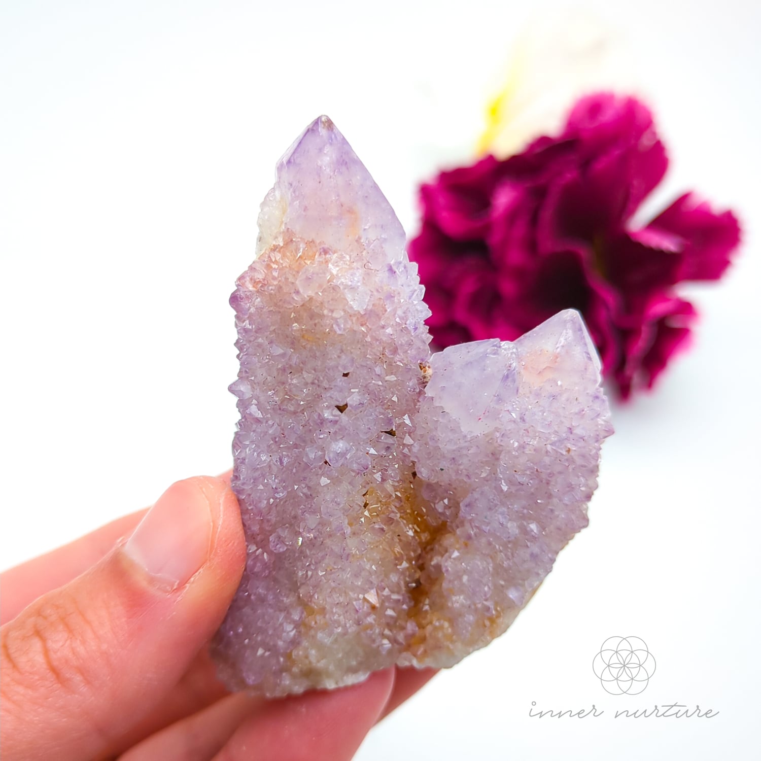 Crystal rock held in a hand with a blurred pink flower in the background. Spirit Quartz cluster for sale at Inner Nurture, an online crystal shop in Australia. 