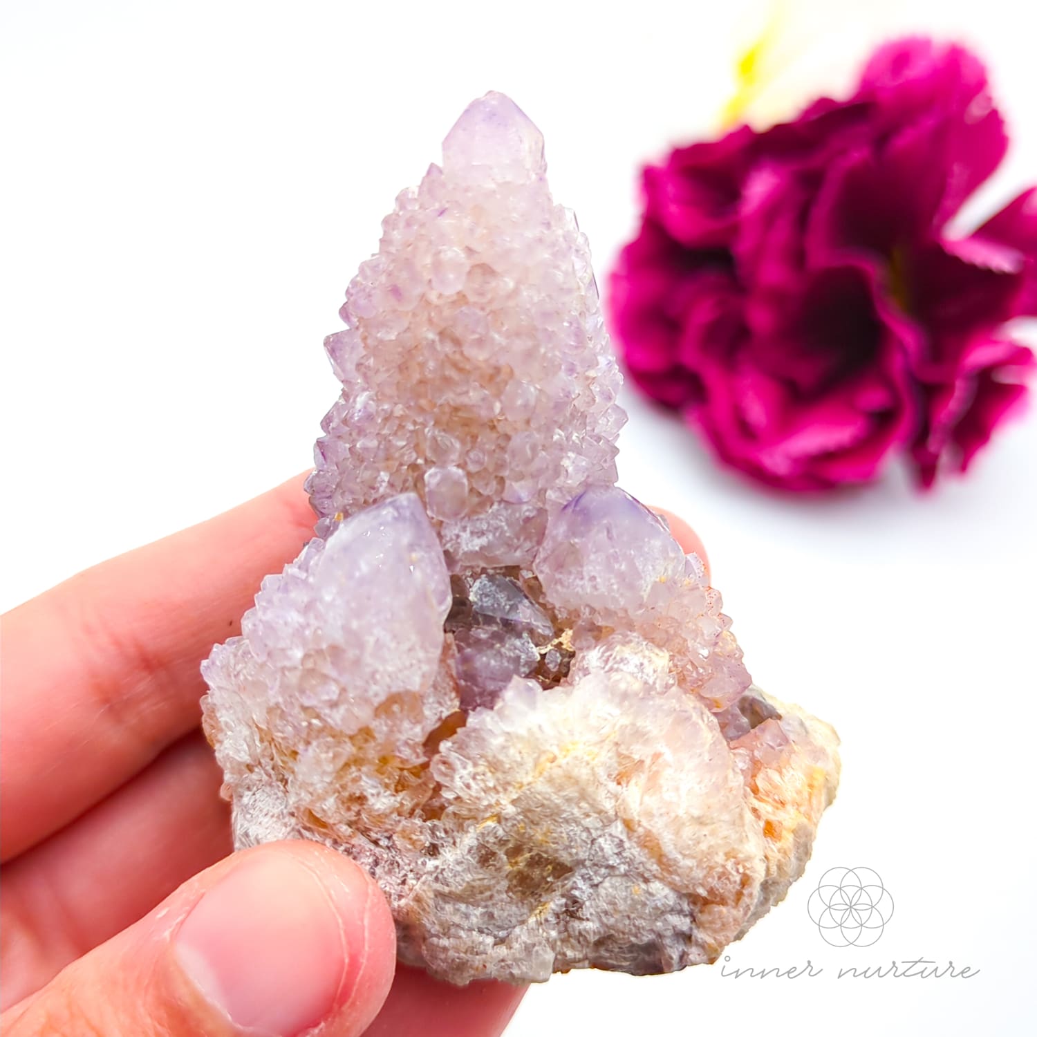 Crystal rock held in a hand with a blurred pink flower in the background. Spirit Quartz cluster for sale at Inner Nurture, an online crystal shop in Australia. 