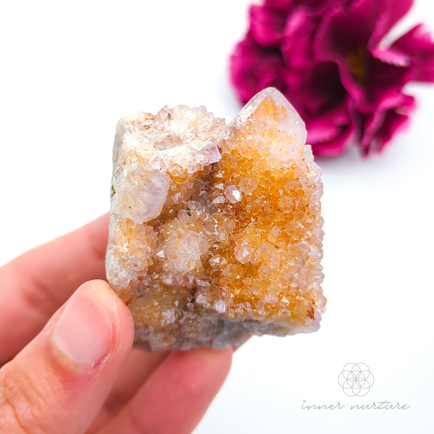 Crystal rock held in a hand with a blurred pink flower in the background. Spirit Quartz cluster for sale at Inner Nurture, an online crystal shop in Australia. 
