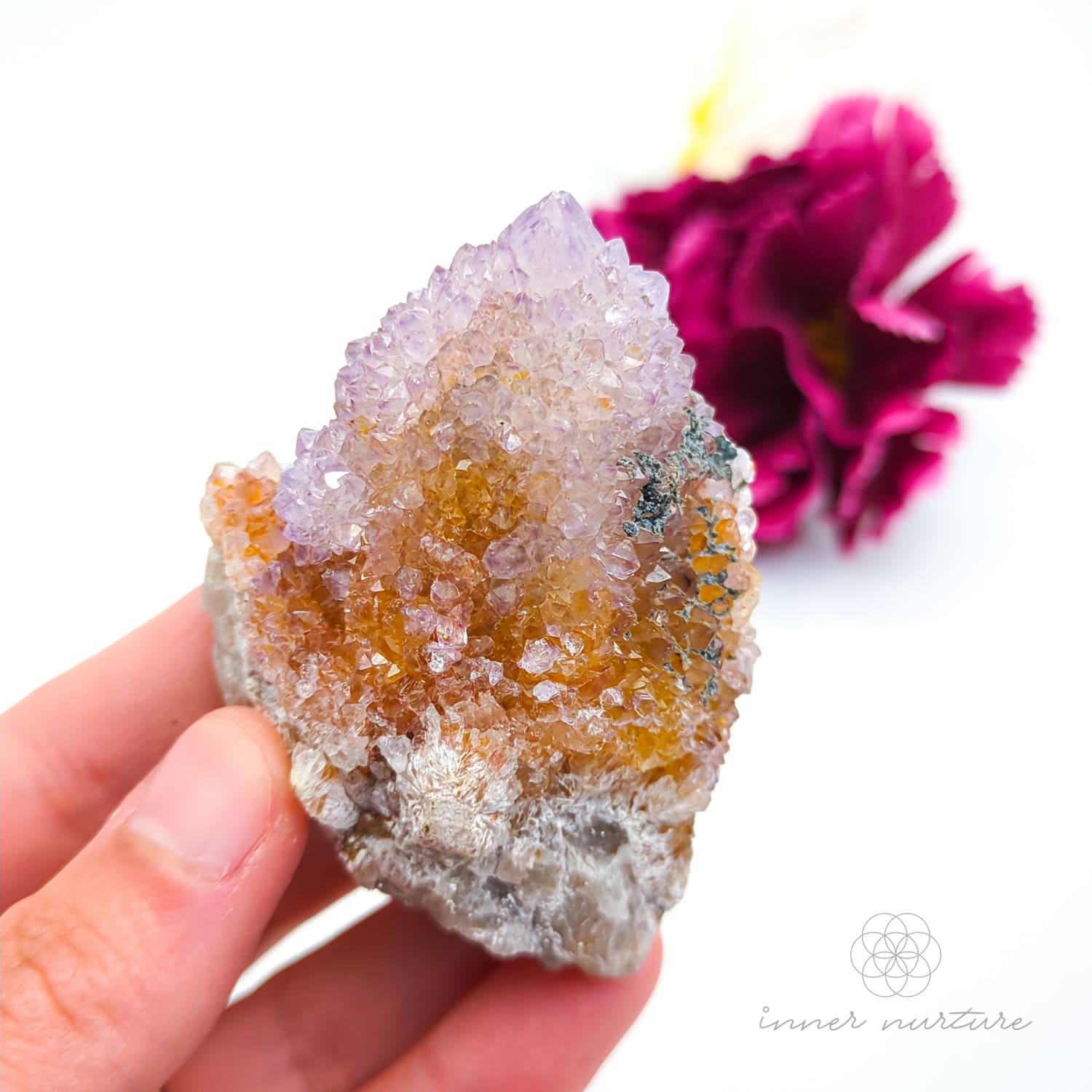 Crystal rock held in a hand with a blurred pink flower in the background. Spirit Quartz cluster for sale at Inner Nurture, an online crystal shop in Australia. 