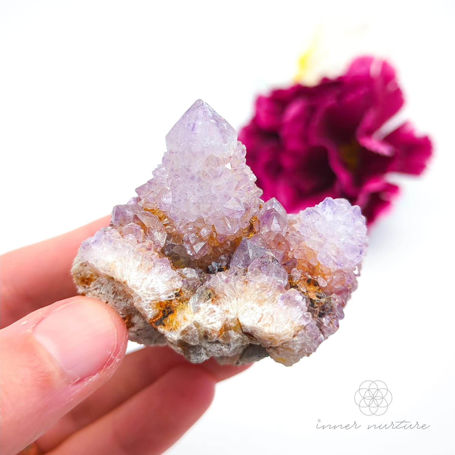 Crystal rock held in a hand with a blurred pink flower in the background. Spirit Quartz cluster for sale at Inner Nurture, an online crystal shop in Australia. 