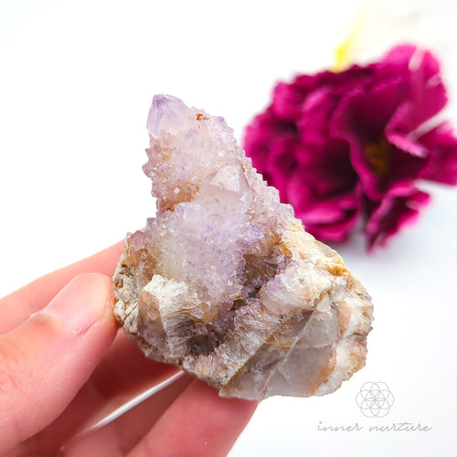 Crystal rock held in a hand with a blurred pink flower in the background. Spirit Quartz cluster for sale at Inner Nurture, an online crystal shop in Australia. 