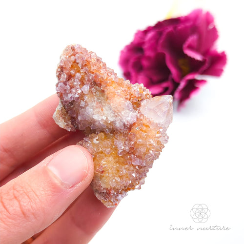 Crystal rock held in a hand with a blurred pink flower in the background. Spirit Quartz cluster for sale at Inner Nurture, an online crystal shop in Australia. 