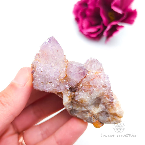 Crystal rock held in a hand with a blurred pink flower in the background. Spirit Quartz cluster for sale at Inner Nurture, an online crystal shop in Australia. 
