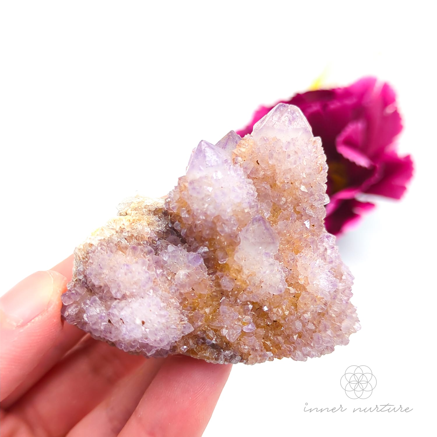 Crystal rock held in a hand with a blurred pink flower in the background. Spirit Quartz cluster for sale at Inner Nurture, an online crystal shop in Australia. 