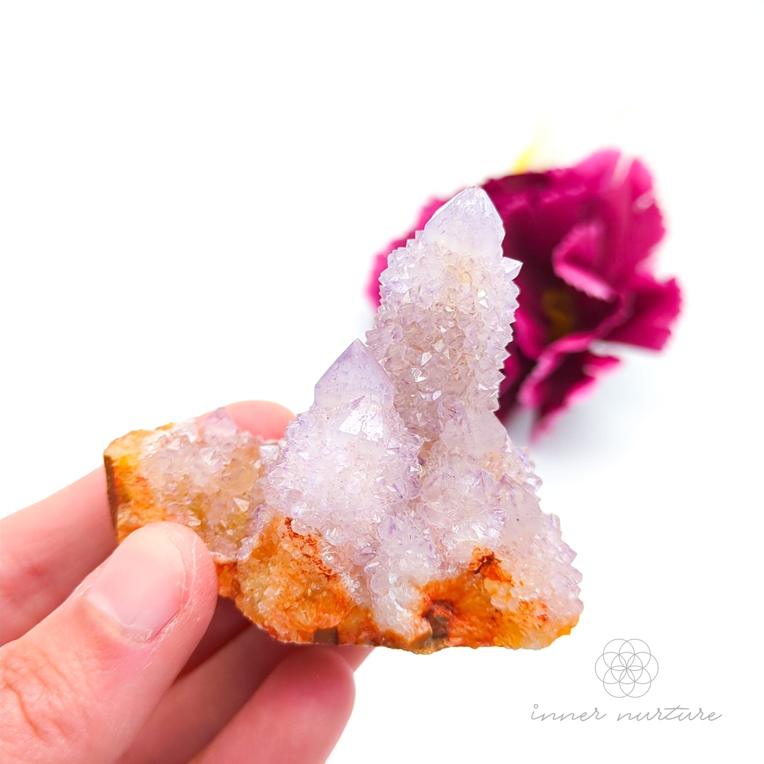 Crystal rock held in a hand with a blurred pink flower in the background. Spirit Quartz cluster for sale at Inner Nurture, an online crystal shop in Australia. 