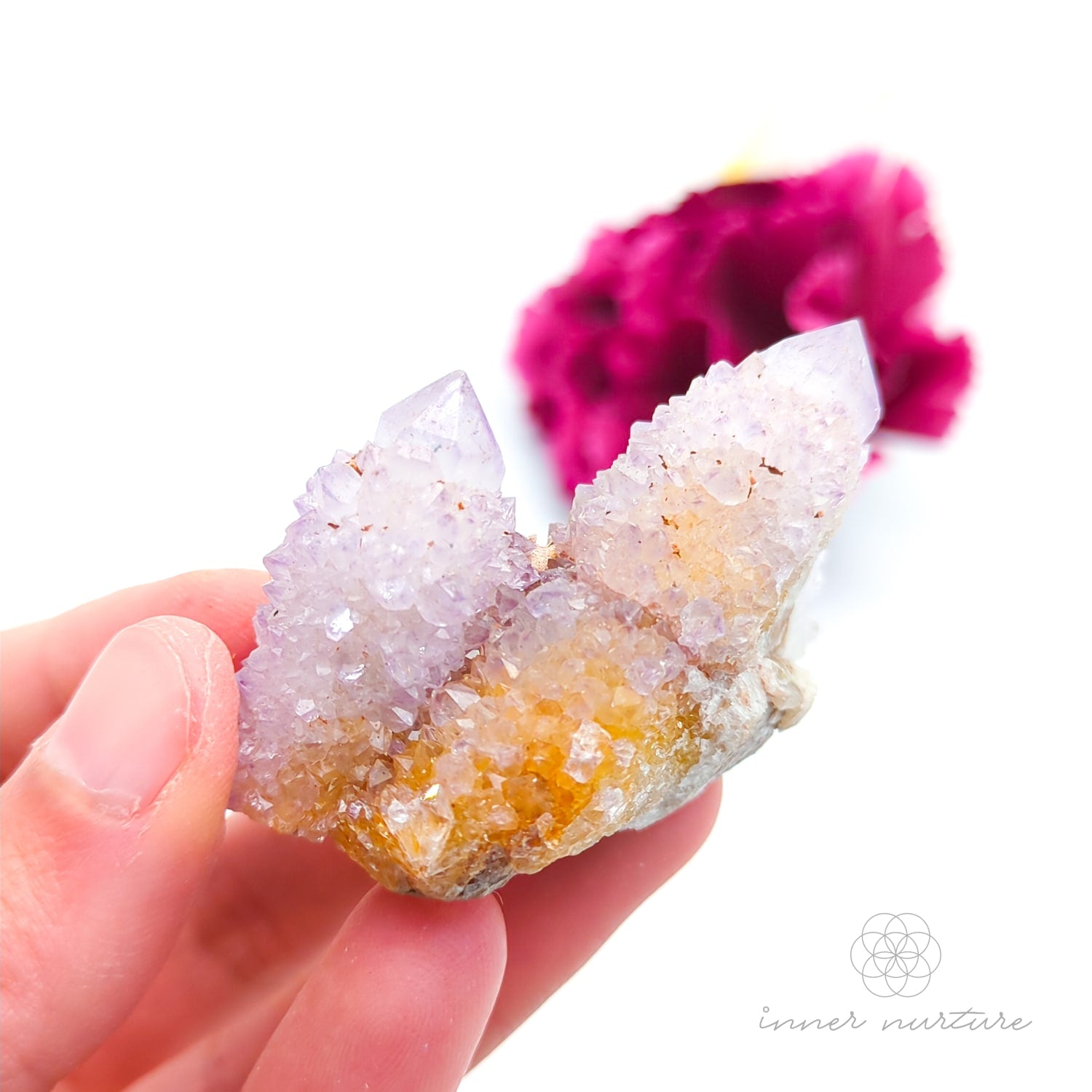 Crystal rock held in a hand with a blurred pink flower in the background. Spirit Quartz cluster for sale at Inner Nurture, an online crystal shop in Australia. 