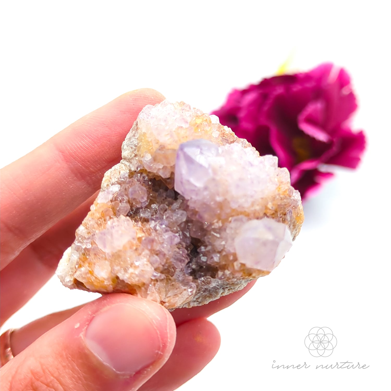 Crystal rock held in a hand with a blurred pink flower in the background. Spirit Quartz cluster for sale at Inner Nurture, an online crystal shop in Australia. 
