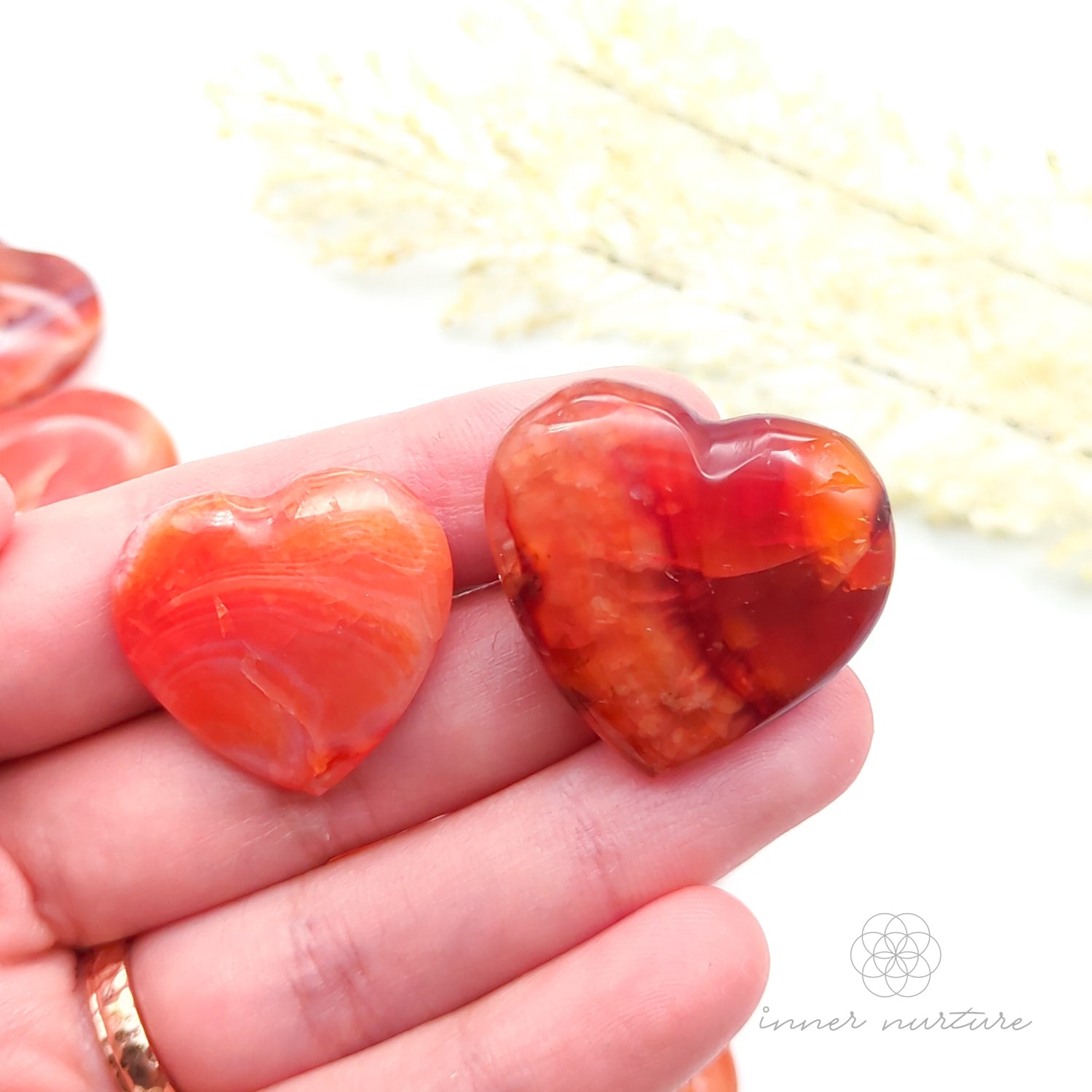 Carnelian crystal hearts held in a hand with yellow flowers in the backdrop. Sold at Inner Nurture, an online crystal shop in Australia. 