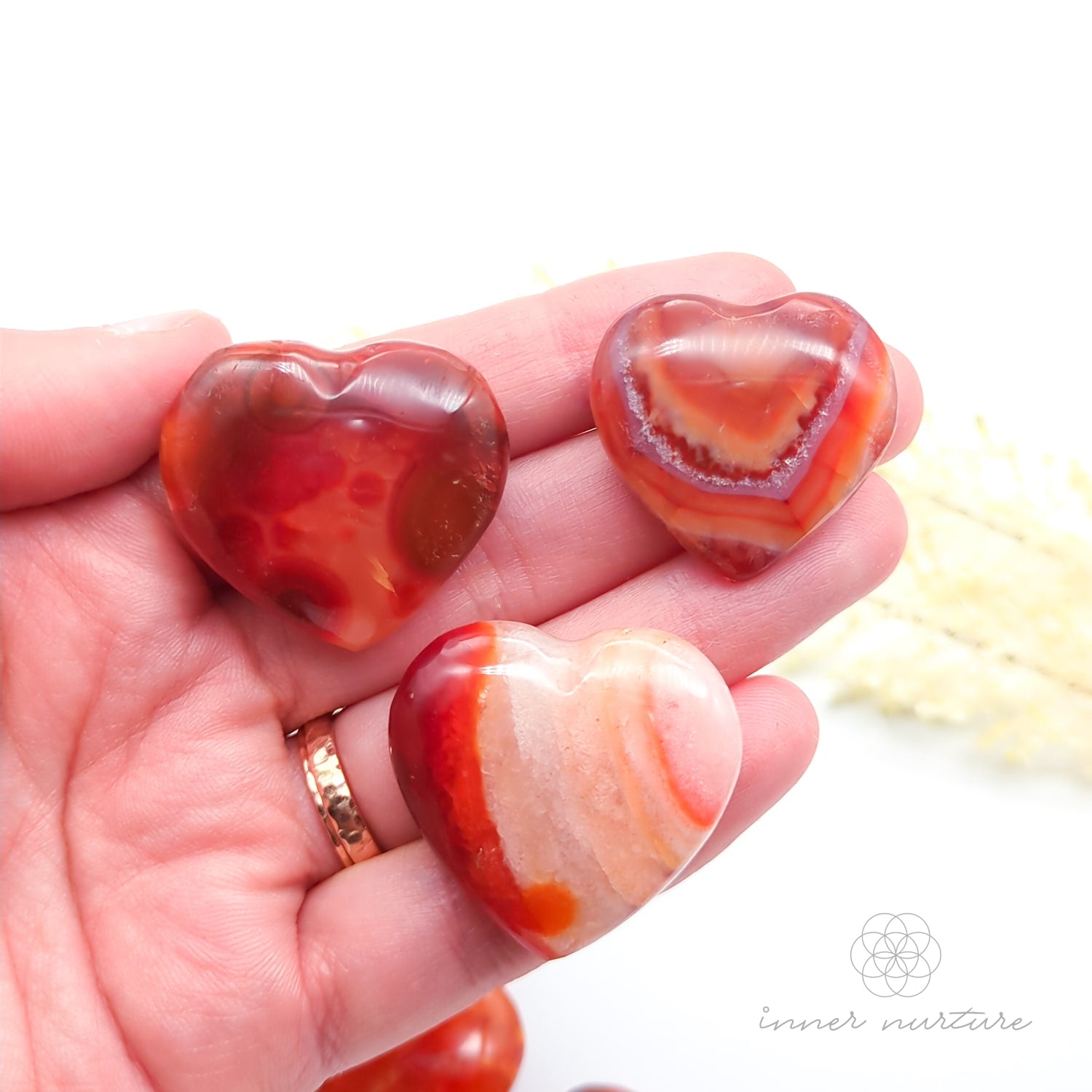 Carnelian crystal hearts held in a hand with yellow flowers in the backdrop. Sold at Inner Nurture, an online crystal shop in Australia. 