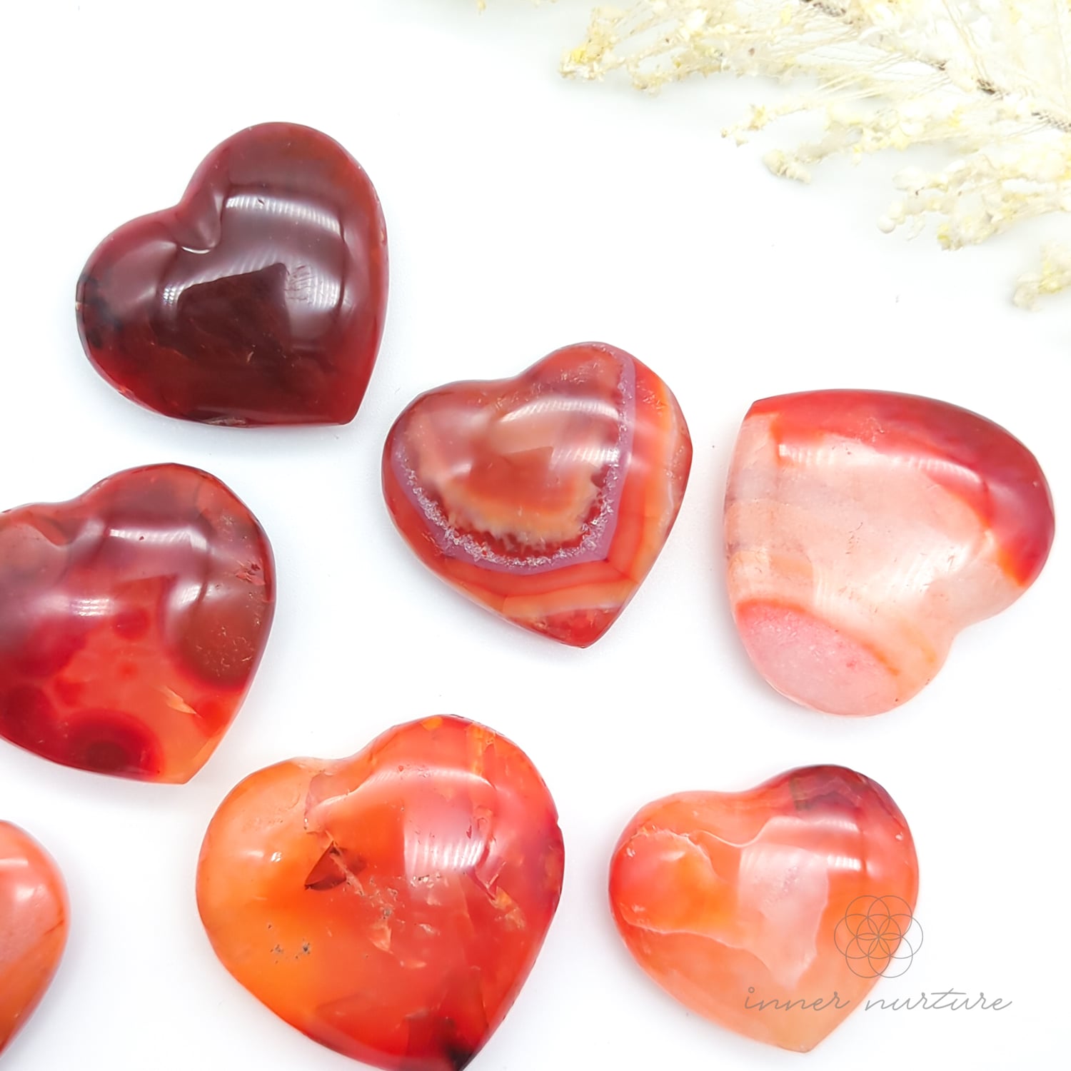 Carnelian crystal hearts on a white backdrop with yellow flowers in the backdrop. Sold at Inner Nurture, an online crystal shop in Australia. 