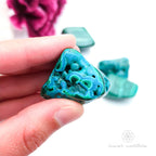 Blue green stone held in hand, with more stones in the background and a white and purple flower. Malacolla sold at Inner Nurture, an online crystal shop in Australia. 