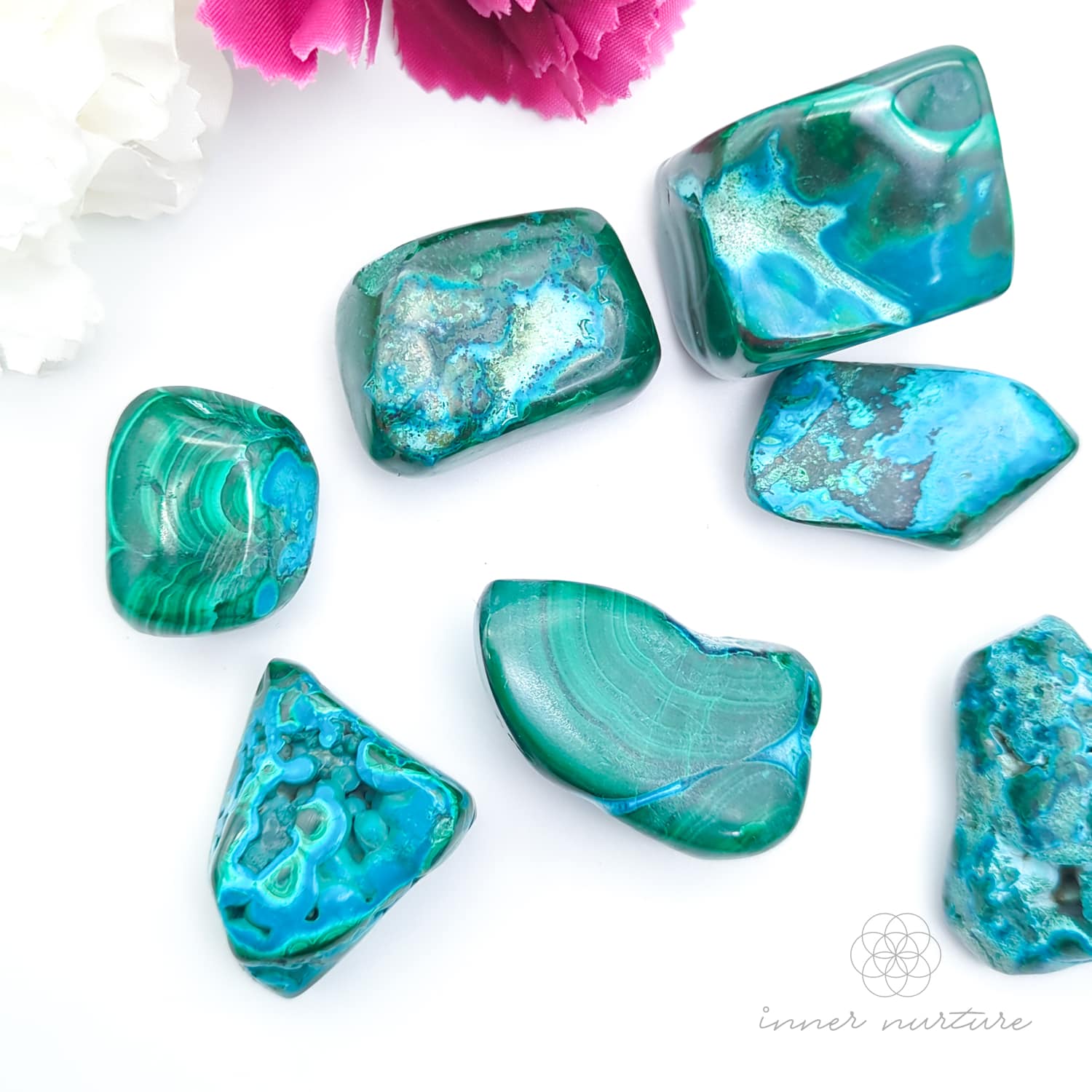 Blue green stone held in hand, with more stones in the background and a white and purple flower. Malacolla sold at Inner Nurture, an online crystal shop in Australia. 