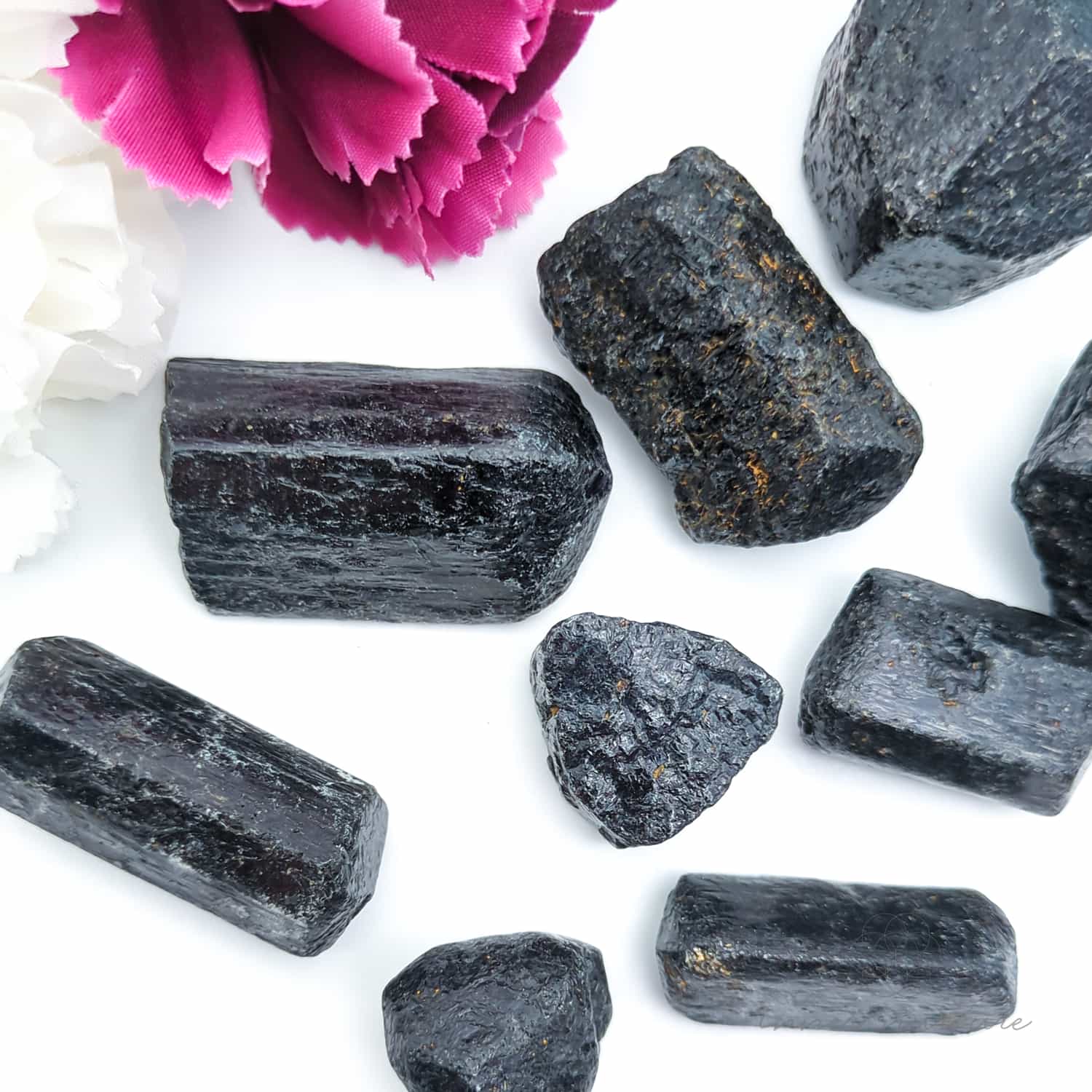 Black crystals on a white surface with a pink flower in the background. Available online at Inner Nurture, an Australian crystal store. 