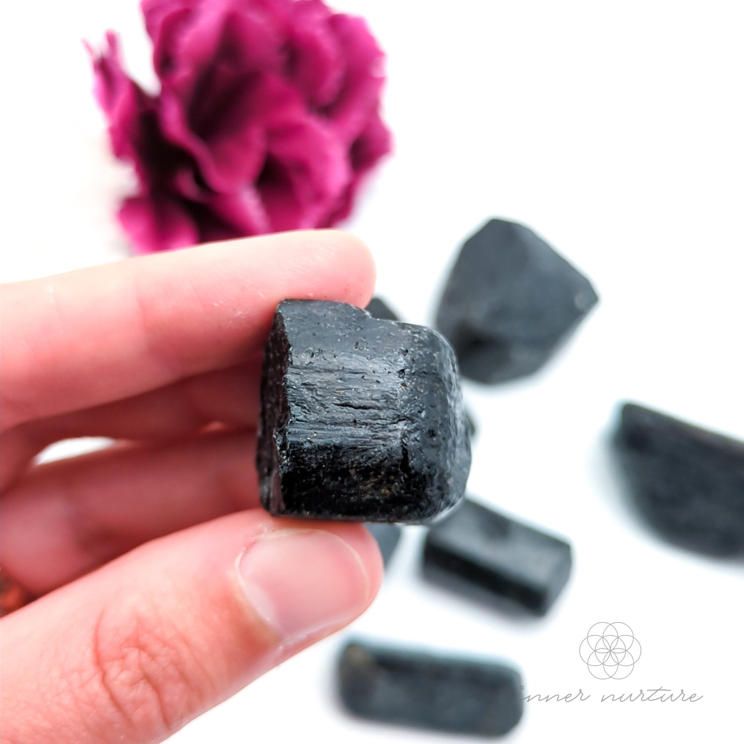 Hand holding a dark crystal with pink flowers in the background. Black Tourmaline available online at Inner Nurture, an Australian crystal store. 