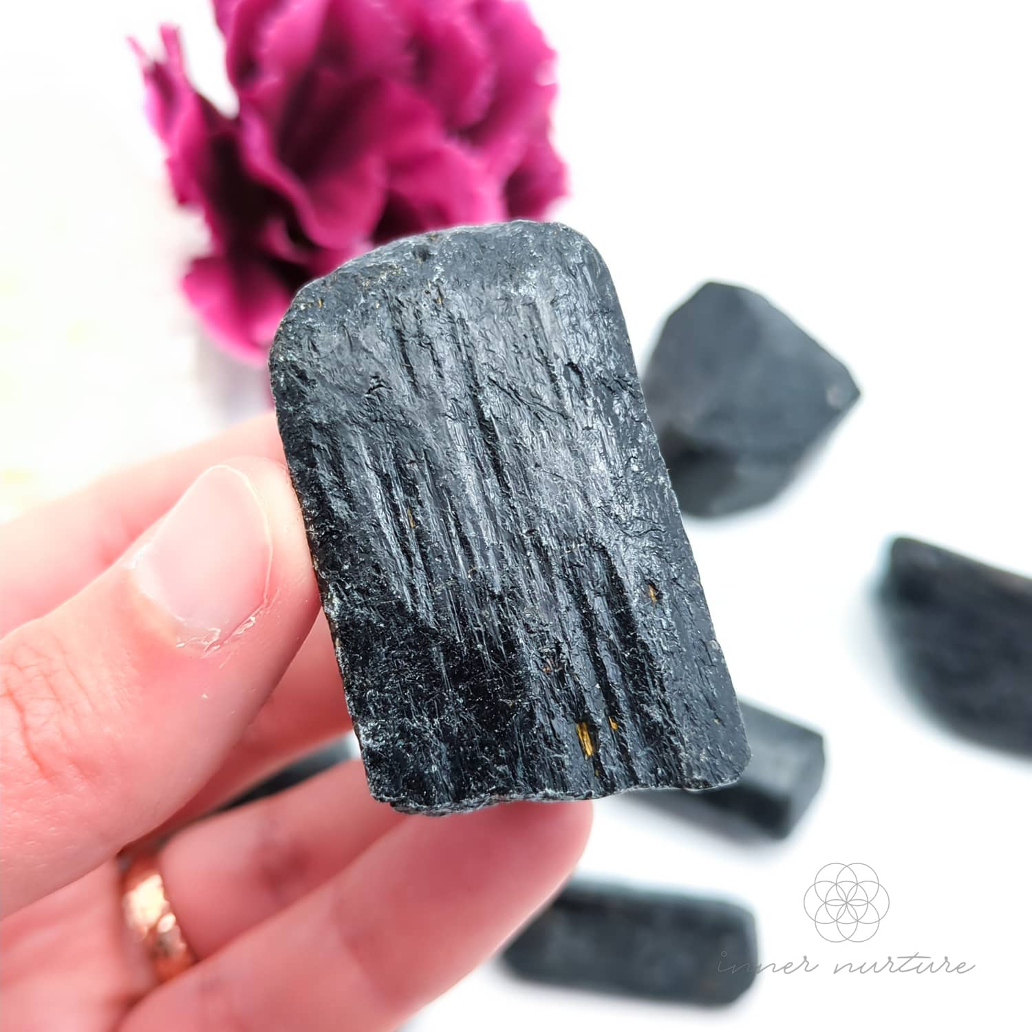 Hand holding a dark crystal with pink flowers in the background. Black Tourmaline available online at Inner Nurture, an Australian crystal store. 
