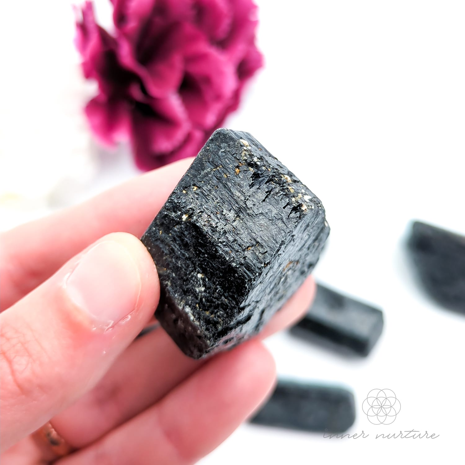 Hand holding a dark crystal with pink flowers in the background. Black Tourmaline available online at Inner Nurture, an Australian crystal store. 