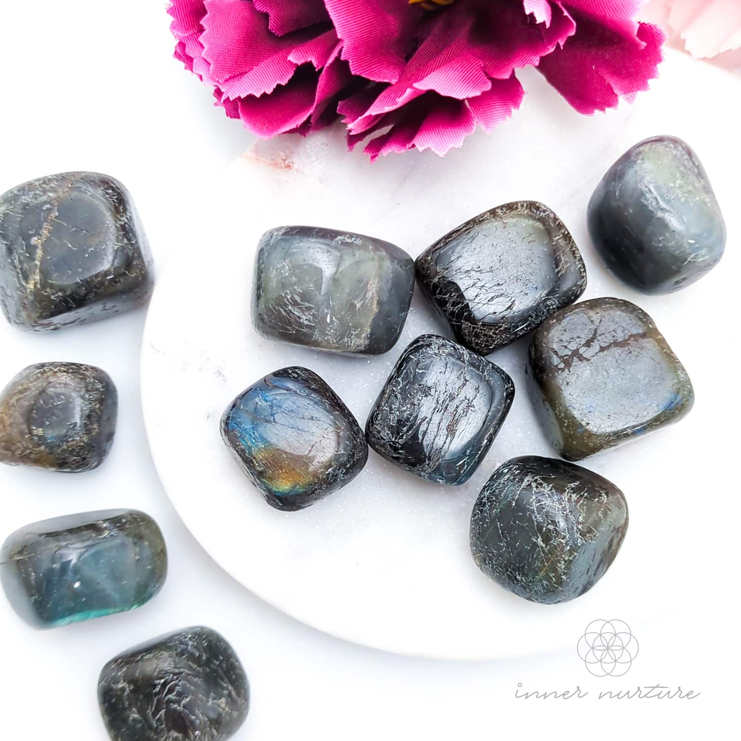 Labradorite semi-polished tumbles with a white background and pink flower. Sold online in Australia at Inner Nurture. 