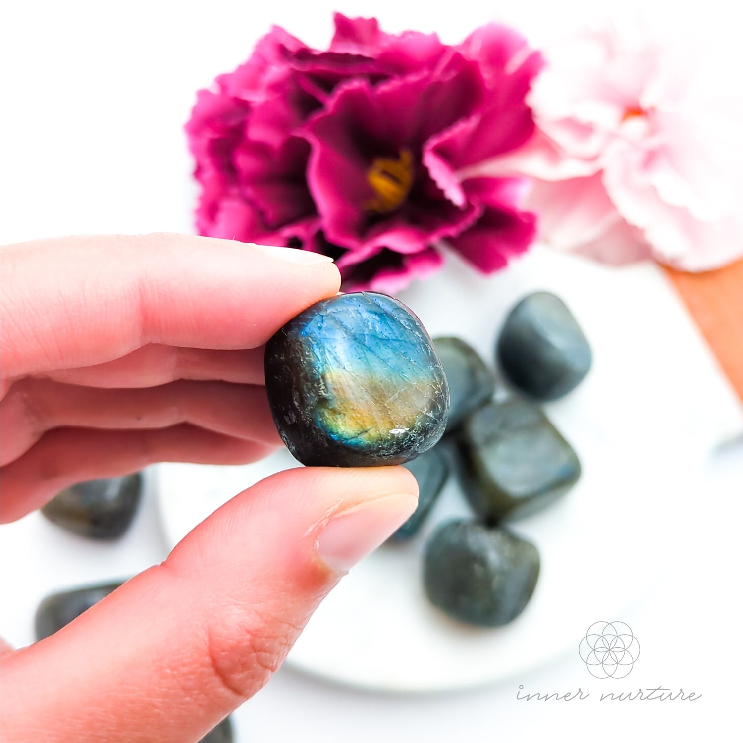 Hand holding a labradorite stone with flowers in the background. Sold online in Australia at Inner Nurture