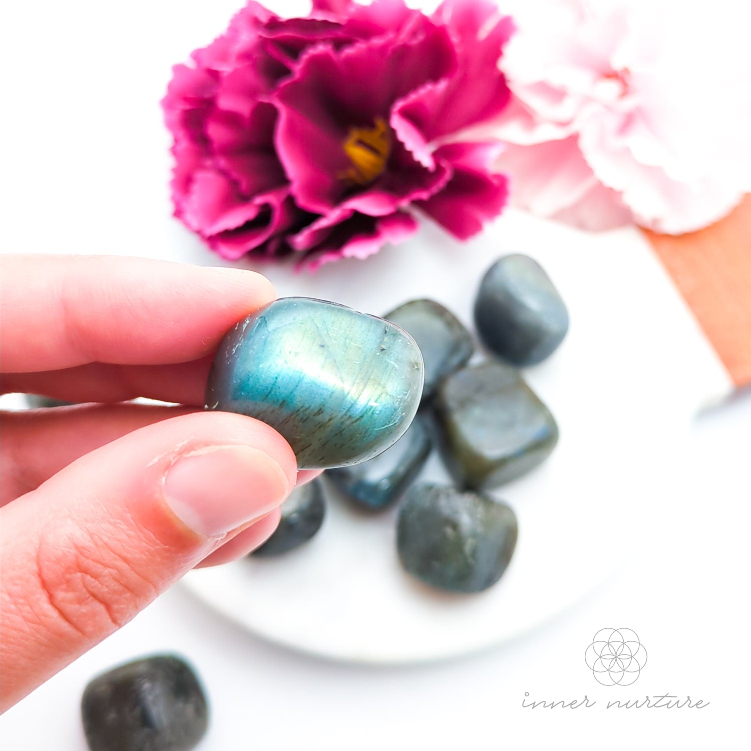 Hand holding a labradorite stone with flowers in the background. Sold online in Australia at Inner Nurture