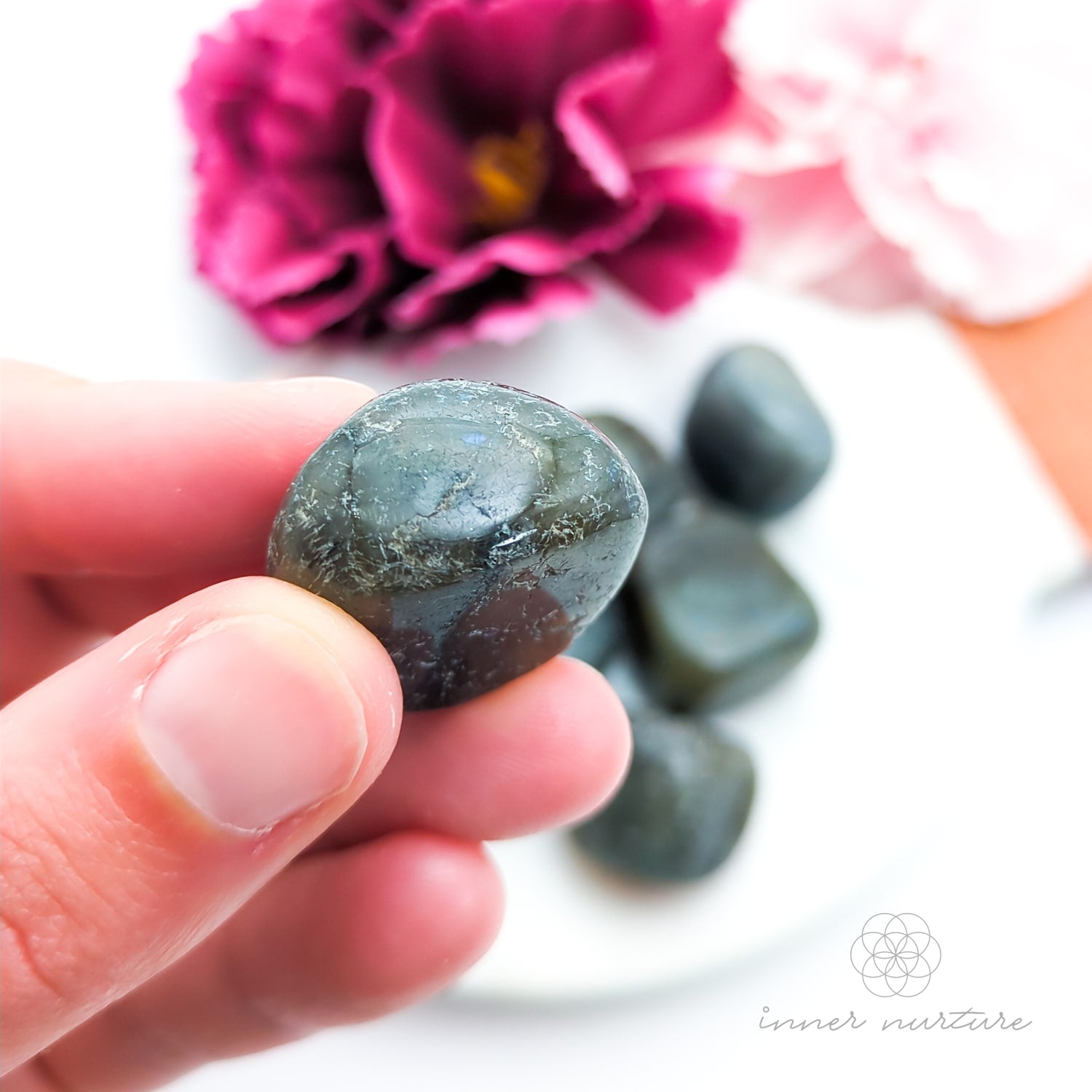 Hand holding a labradorite stone with flowers in the background. Sold online in Australia at Inner Nurture