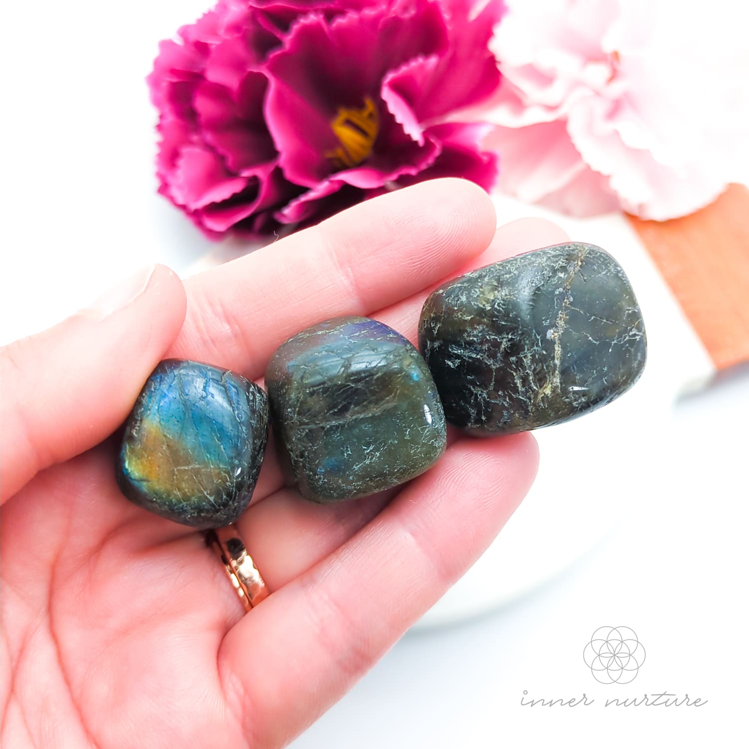 Hand holding a labradorite stone with flowers in the background. Sold online in Australia at Inner Nurture