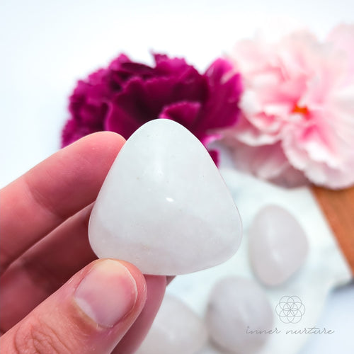 Hand holding a white stone with flowers in the background. Rose Quartz Tumble - Inner Nurture | Crystal Shop Australia 