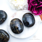 Hand holding a labradorite stone with a pink flower in the background. Labradorite stones available to buy from Inner Nurture, an online crystal shop in australia.