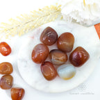 Polished agate stones on a white plate with decorative elements. Carnelian tumbles available at Inner Nurture, an online crystal shop in Australia.