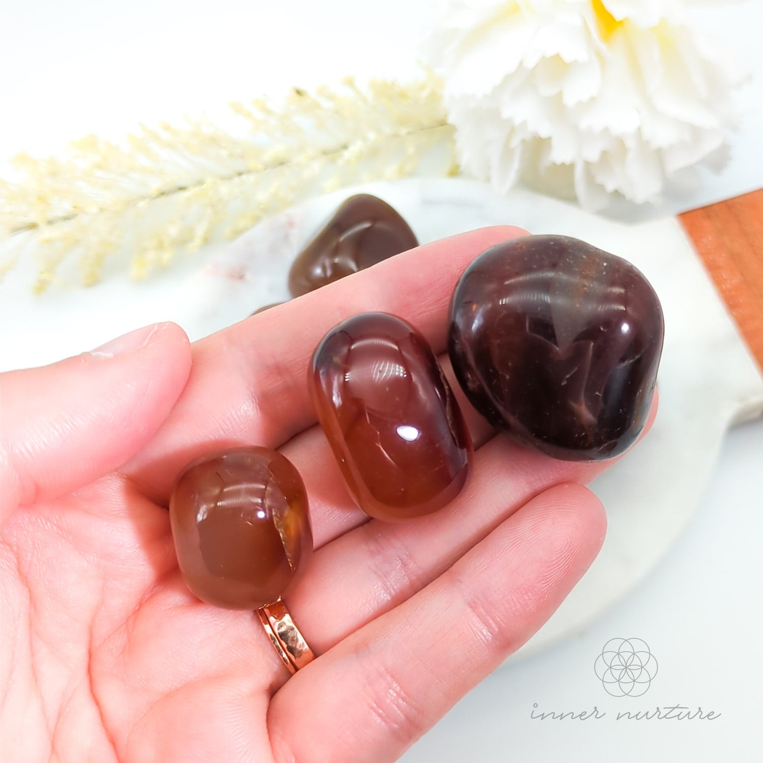 Hand holding three brown stones with a blurred natural background. Carnelian tumbles available at Inner Nurture, an online crystal shop in Australia.