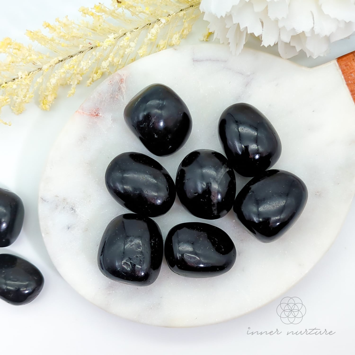 Black stones on a white plate with decorative elements. Black Tourmaline tumbles available at Inner Nurture, an online crystal shop in Australia.